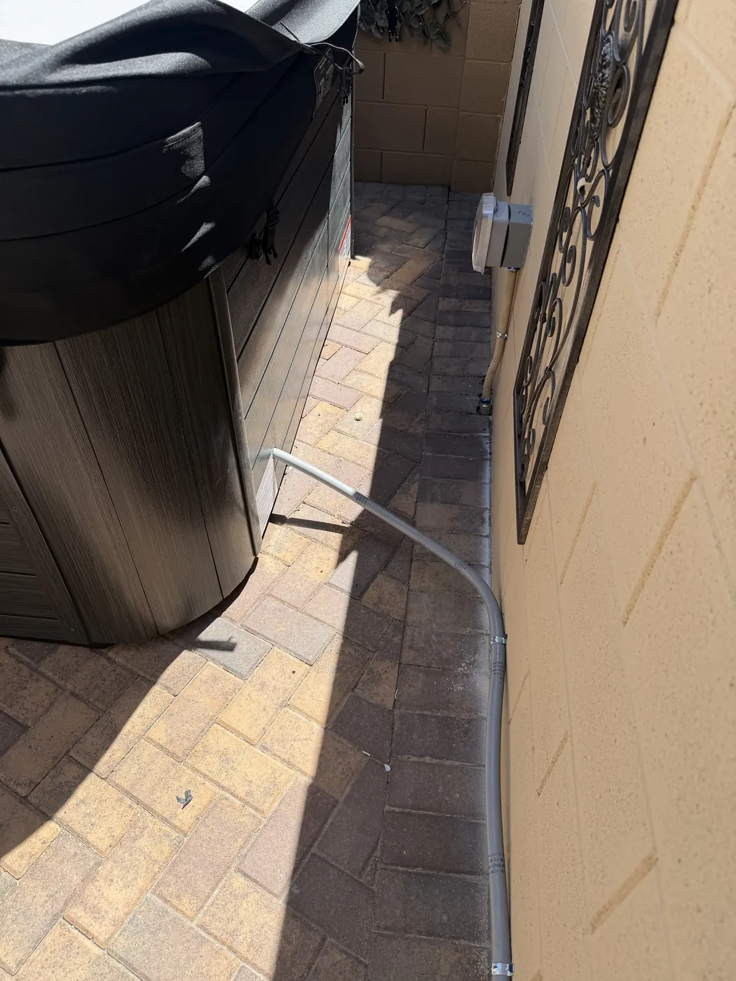 Electrical conduit run along a stucco wall beside a paver walkway