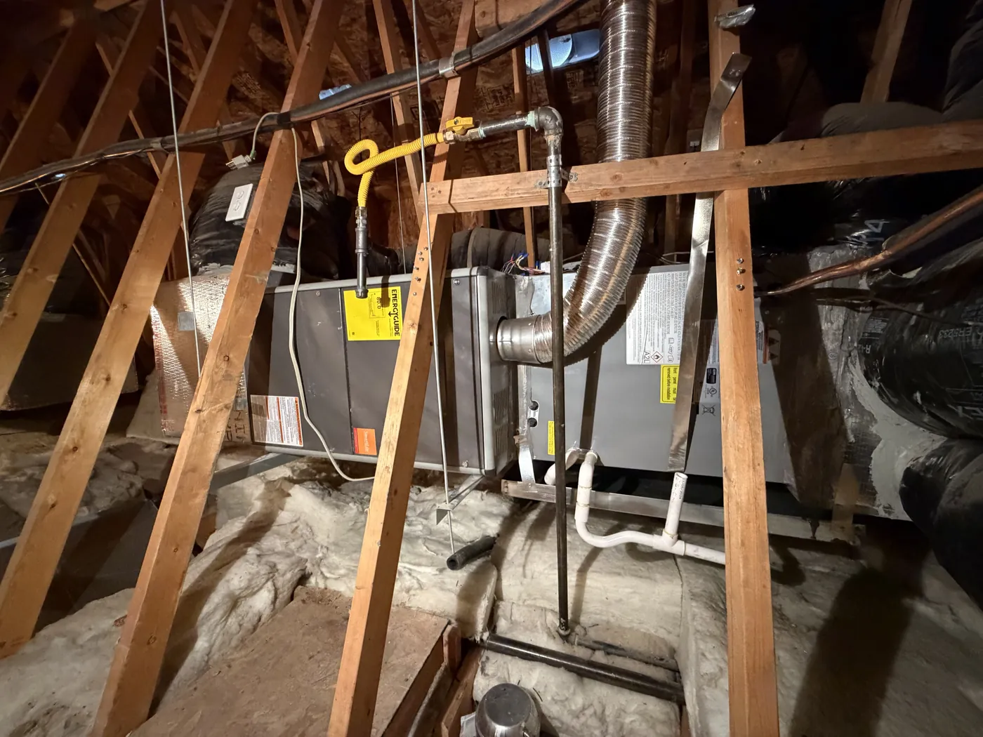 Attic air handler with refrigerant lines and condensate drain between roof trusses