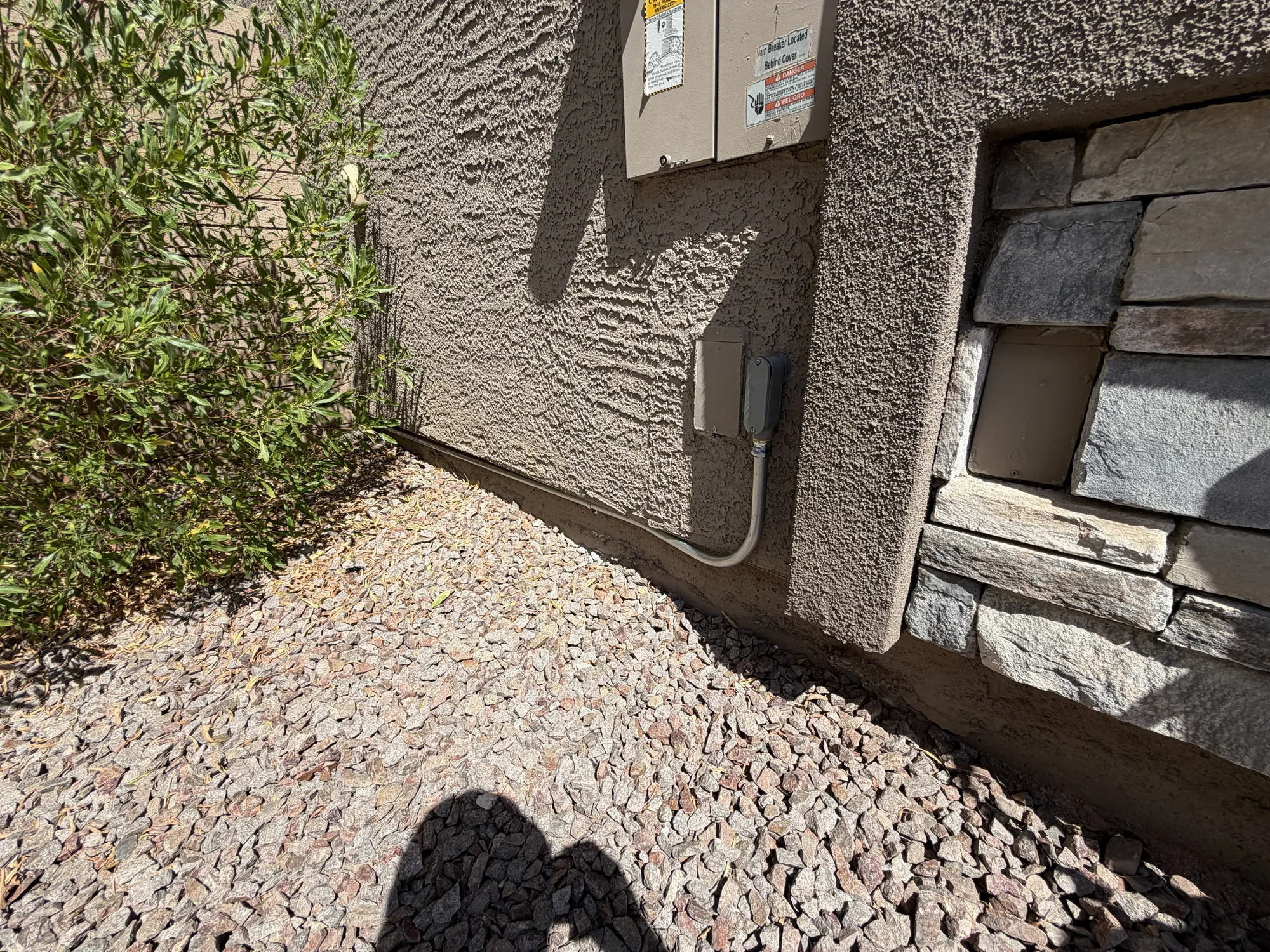 Electrical conduit and meter box run along a stucco wall beside a stacked stone accent