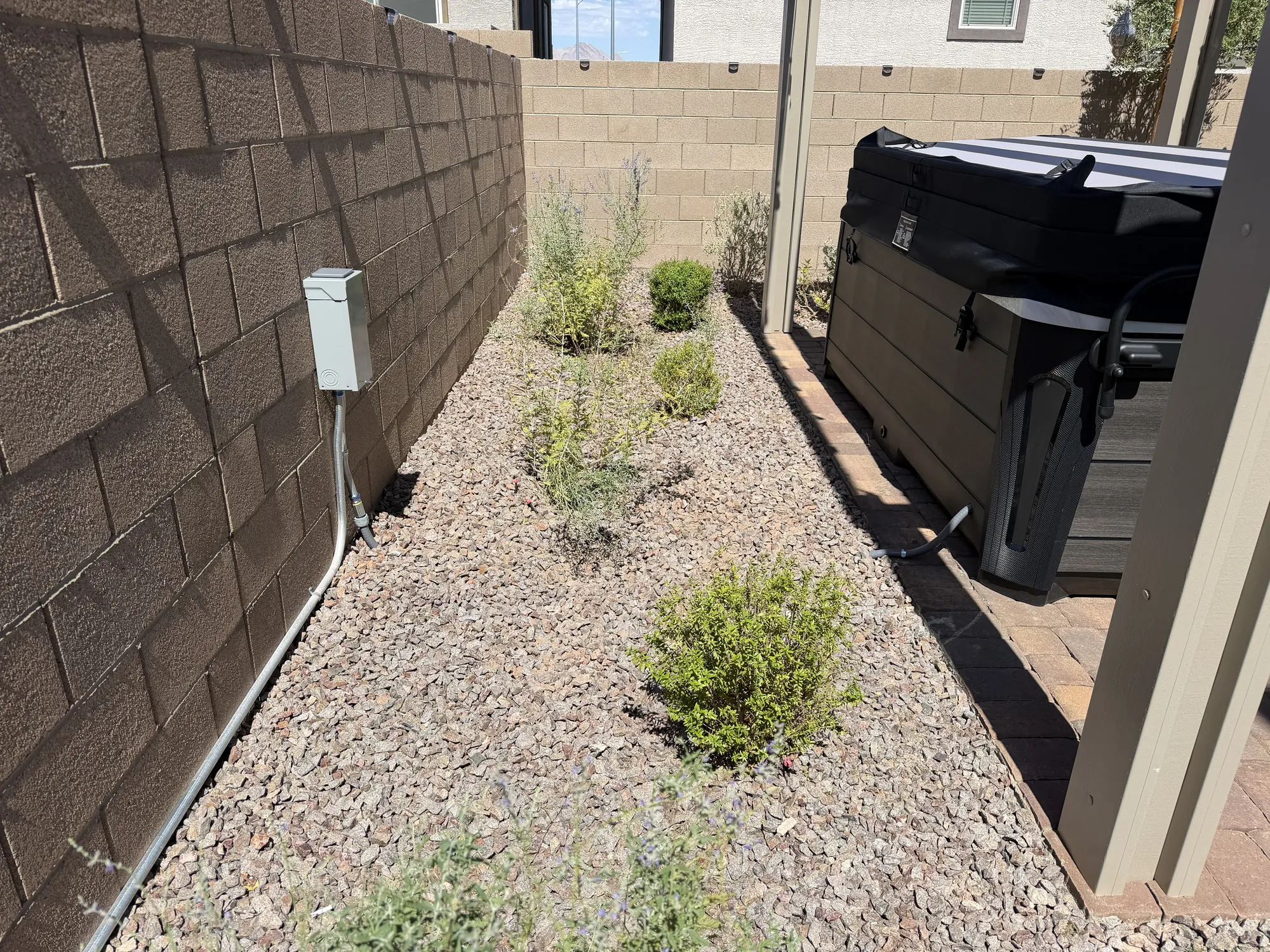 Metal conduit running along a paved side yard next to a covered spa