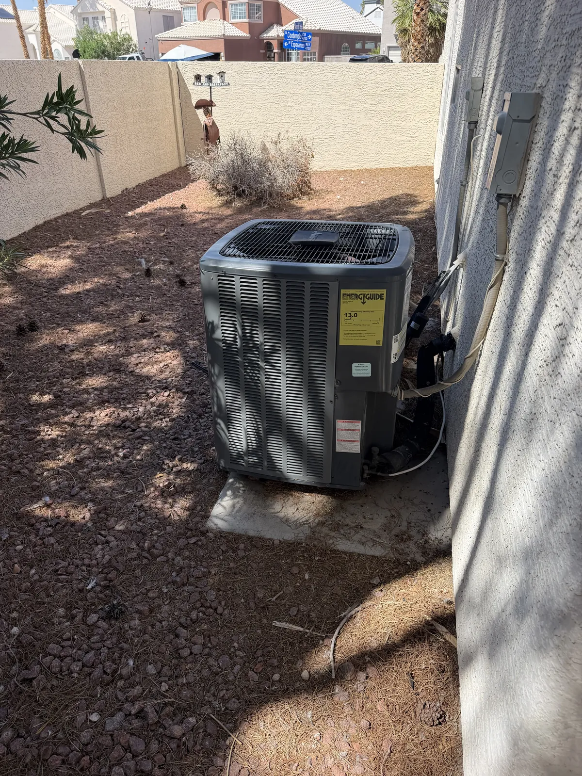 Outdoor air conditioner condenser installed beside a stucco wall on a gravel pad